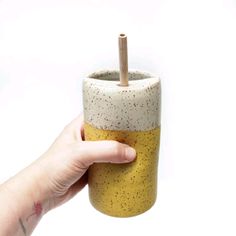 a hand holding a cup with a wooden stick sticking out of it's top