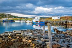 there are many boats in the water near some rocks and wood posts on the shore