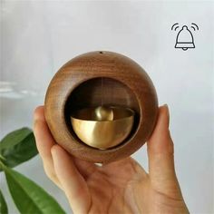 a hand holding a wooden object with a bell in it