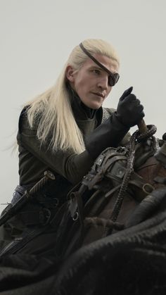 a woman with long blonde hair sitting on top of a horse wearing black leather gloves