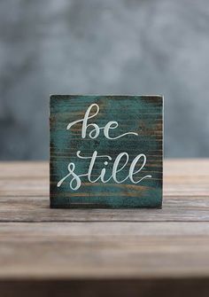 a wooden block with the words be still written in white ink on top of it