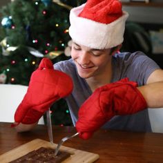 a man in a santa hat is cutting chocolate on a table with red mittens