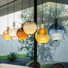 several different colored lights hanging from the ceiling above a dining room table with brown chairs