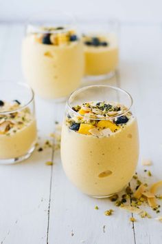 three glasses filled with dessert sitting on top of a white wooden table next to each other