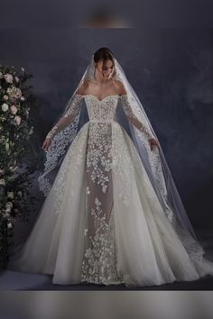 a woman in a wedding dress with a veil on her head and flowers behind her