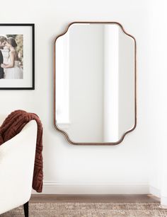 a white chair sitting in front of a mirror on the wall next to a framed photo