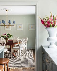 a dining room table with white chairs and flowers in a vase on the wall behind it