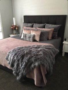 a bedroom with grey and pink bedding, pillows and blankets on the headboard