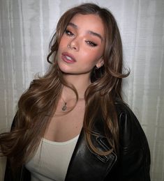 a woman with long brown hair wearing a black leather jacket and white tank top is posing for the camera