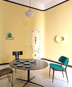 a dining room with yellow walls and blue chairs on the floor, along with a round glass table