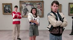 three people are standing in front of paintings and one is holding his arms crossed while the other looks at the camera