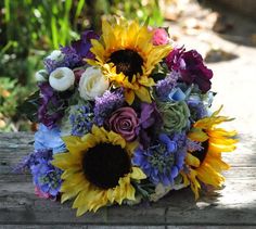 a bouquet of sunflowers and other flowers on a wooden table in a garden