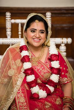 a woman in a red and gold sari sitting on a chair with flowers around her neck