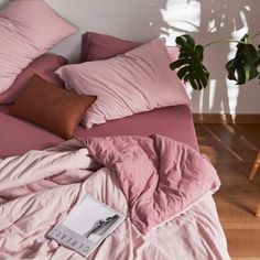 a bed with pink sheets and pillows on top of it next to a potted plant