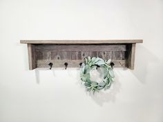 a wooden shelf with a wreath hanging from it's side and hooks on the wall