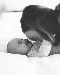 a woman holding a baby in her arms while laying on top of a white bed