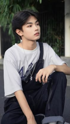 a young man sitting on the ground wearing overalls