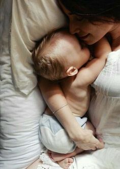 a woman holding a baby in her arms while laying on top of a white bed