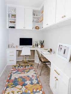 a white desk with a computer on top of it next to a rug and cabinets