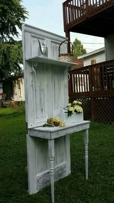 an old cabinet is painted white and has flowers on it in the grass near a house