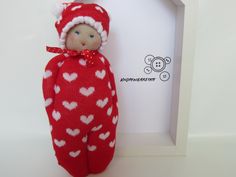 a red and white knitted doll with hearts on it's body next to a box