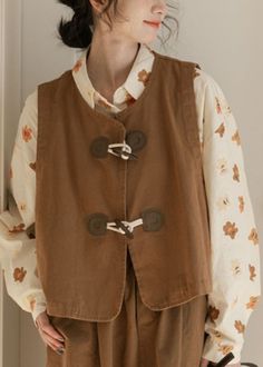 a woman standing in front of a door wearing a brown vest