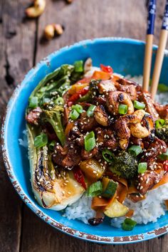 a blue bowl filled with rice, broccoli and other food on top of a wooden table