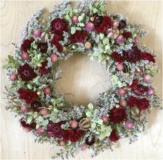 a wreath with red flowers and greenery on a wooden surface, ready to be hung