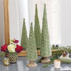 three small green trees sitting on top of a table next to a mirror and flowers