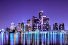 the city is lit up at night and reflecting in the water