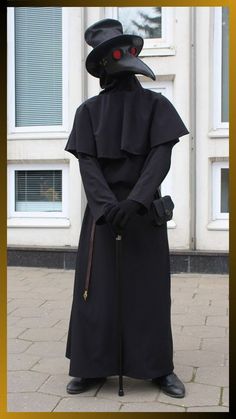 a man in a black outfit and hat with a cane standing on the sidewalk next to a building