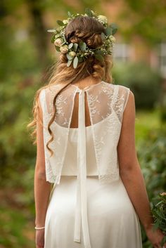 the back of a woman wearing a white dress with a flower crown on her head