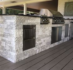 an outdoor kitchen built into the side of a house with grills and ovens