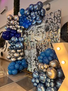 blue and silver balloons are hanging from the ceiling in front of a wall with an image on it