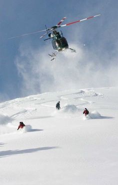 skiers are skiing down a snowy mountain with a helicopter flying above them and onlookers below