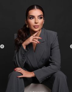 a woman sitting on top of a chair wearing a gray suit and matching heels with her hand under her chin