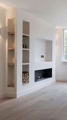 an empty living room with white walls and wood floors, fireplace in the center surrounded by bookshelves