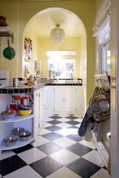 a kitchen with black and white checkered flooring next to an archway leading into the dining room