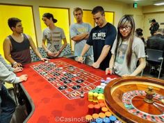 a group of people standing around a rouleet table in a room with yellow walls