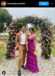 a man and woman standing in front of a floral arch