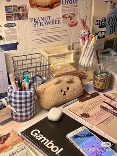 a stuffed animal sitting on top of a desk next to papers and pens in front of a computer monitor