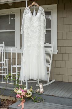 a wedding dress hanging on a porch next to a flower bouquet and bride's shoes