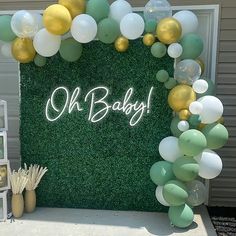 an outdoor baby shower with balloons and greenery on the wall, along with a sign that says oh baby