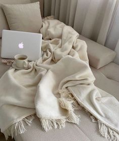 an open laptop computer sitting on top of a white couch next to a cup of coffee