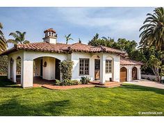 a white house sitting on top of a lush green field with palm trees in the background