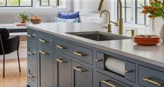 a kitchen with blue cabinets and white counter tops, gold pulls on the faucet