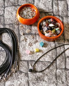 two orange bowls sitting on top of a stone floor next to necklaces and beads