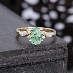 an oval cut green tourmaline and diamond ring on top of a wooden table