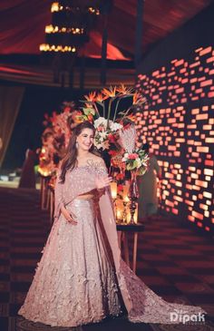 a woman in a pink lehenga standing next to a table with flowers on it