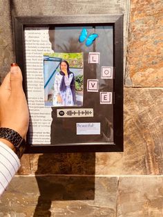 a person holding up a framed photo in front of a stone wall with butterflies on it